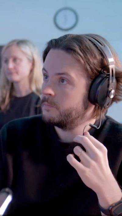 A man in a black top wears a headset and holds the mic part in his hand while he listens to someone
© BBC