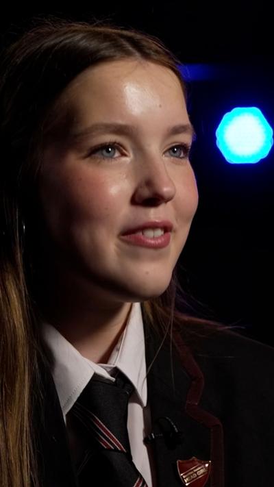 Laura -  pupil with long dark hair wearing school uniform including tie and white shirt