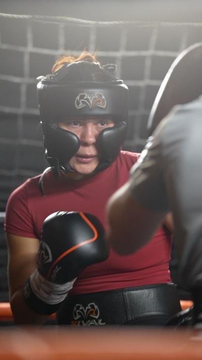 A woman wearing boxing gear photographed sparring in the ring
