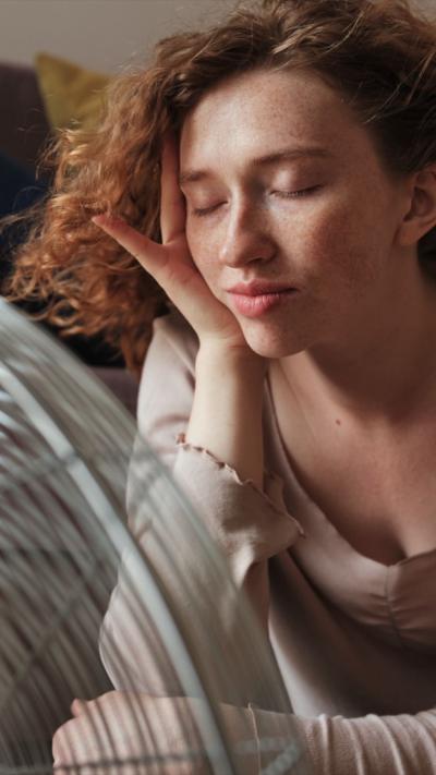 Woman with closed eyes sits in front of a fan as her hair is blown around.