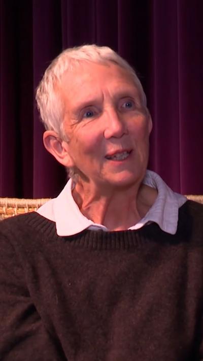 Woman sitting in wicker chair, with purple velvet curtains in the background.