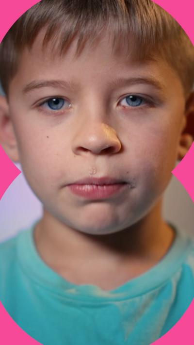 A boy with short light brown hair looks directly into the camera