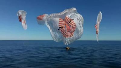 Blue sky with capsule being held up by four parachute-like drogues over the ocean