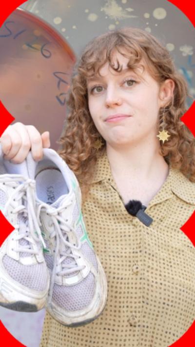 Kate Bowie has long curly red hair, is wearing a yellow shirt and is holding up a purple pair of Rainers in her right hand.