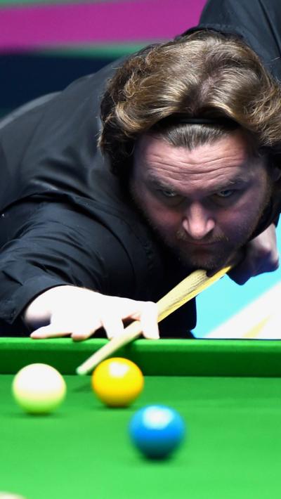 A snooker player with a black outfit and black headband cueing up the white ball from the baulk end of the table