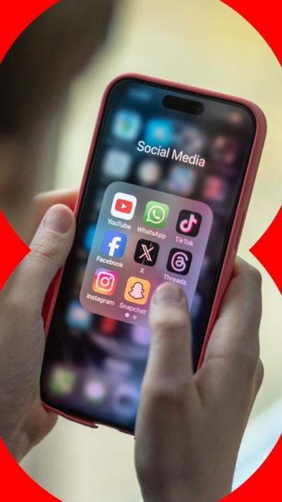A person holding a mobile phone which shows a folder with several social media apps.