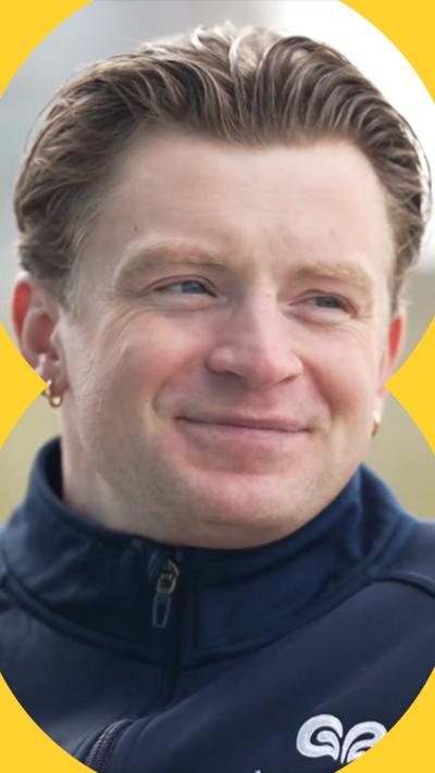 Adam Peaty looks to the side of the camera and smiles. He wears a navy jacket.