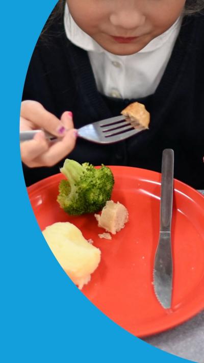 A school-aged child is shown eating a school dinner of a red plate. Only the lower half of their face is visible.