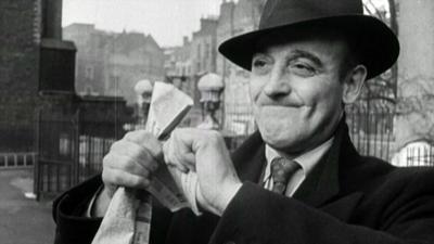 Black and white image of man in coat and hat ripping up a card from his pocket having just read the newspaper saying that rationing had ended.  (There is a suggestion in the report that this may be a blackmarketeer)