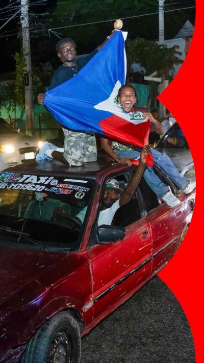 Two men on top of car holding Haiti flag