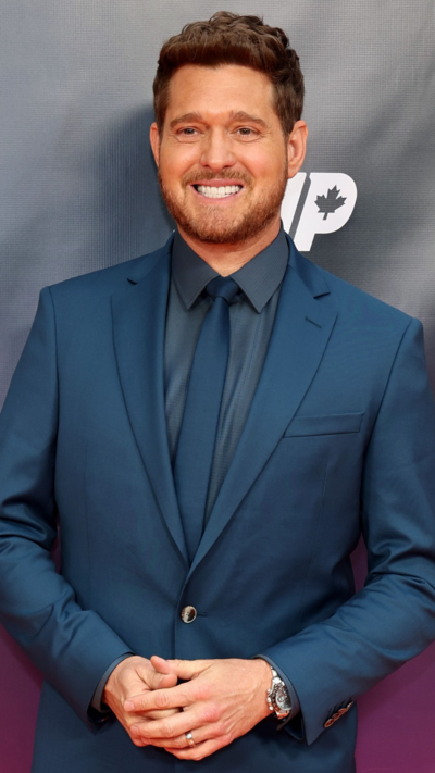 Michael Bublé wearing navy suit, shirt and tie. He has a wide smile on his face.