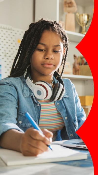 A teenager doing homework. She has headphones around her neck and trophies in the background