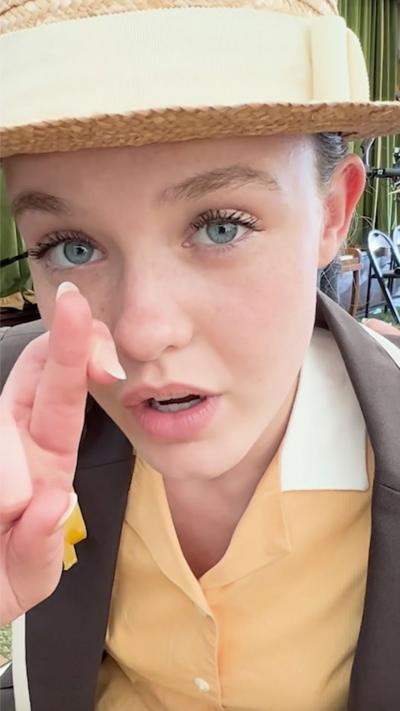 A girl crosses her fingers, she is wearing Malory Towers school uniform which is bright yellow.
