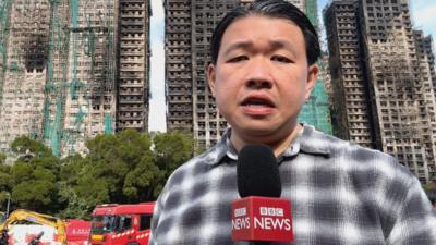 BBC reporter in front of Hong Kong buildings damaged by fire