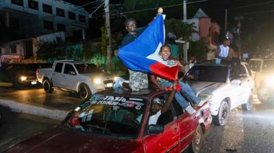 Two men on top of car holding Haiti flag