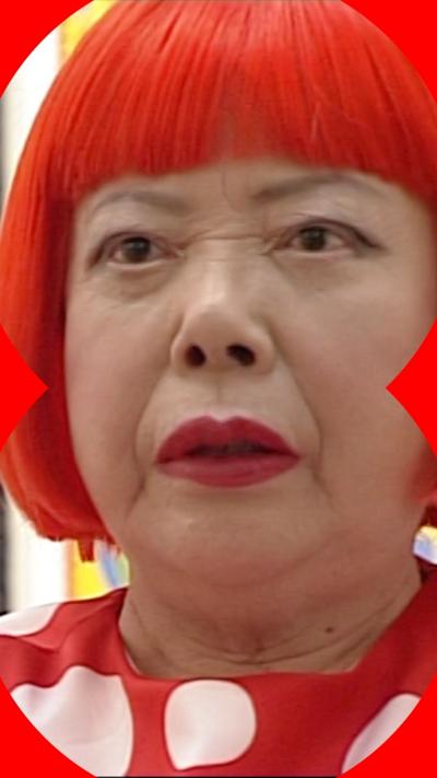 Japanese artist Yayoi Kusama. She is wearing a red dress with large white polka dots and a bright red, bob cut wig.