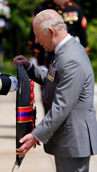The king holds a wreath while wearing a grey suit.