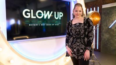 NikkieTutorials is standing in front of a screen that has the words 'Glow Up'
