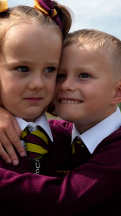 Young boy hugs his twin sister, they are wearing a red and yellow school uniform