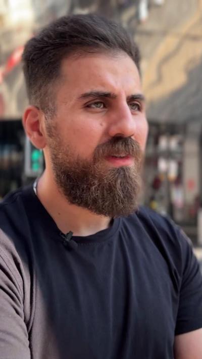 A bearded man with dark hair in a black t-shirt