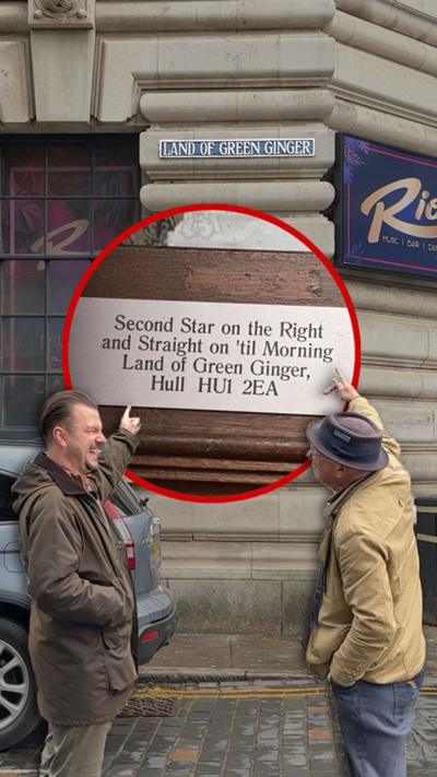 Two men stand on Land of Green Ginger near to a street sign. They are both dressed in outdoor brown coats and are pointing at a superimposed graphic of the magical address Second Star on the Right and Straight on 'til Morning