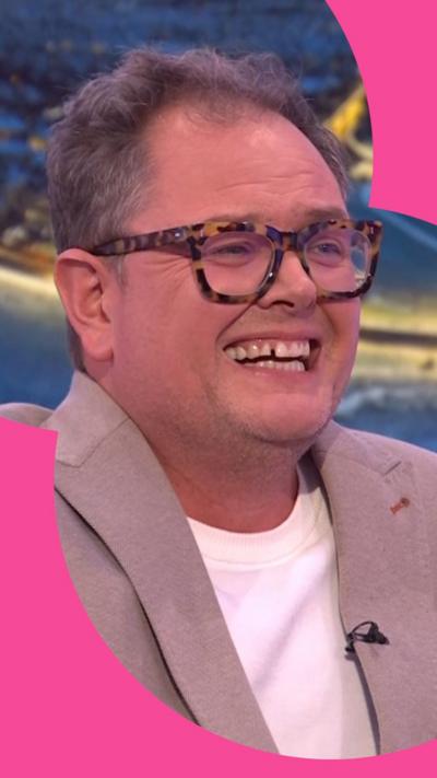Alan Carr in the One Show studio looking to the side and laughing