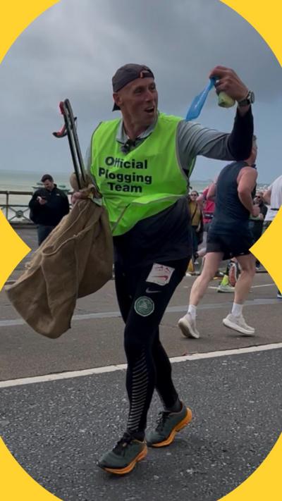 Darren Evans wearing a green bib saying 'official plogging team' whilst running. He looks to his left and holds up litter.