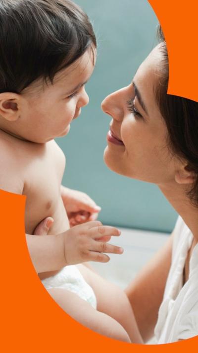Side view: a woman with long dark hair holding her baby who's in a nappy and staring at its face