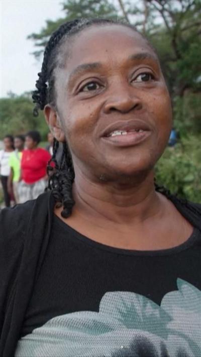 A woman in a black top with a floral design speaks to camera