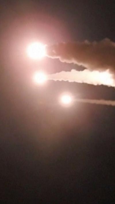 Three missiles seen as bright balls of light streak through a dark night sky leaving behind a trail of grey smoke.