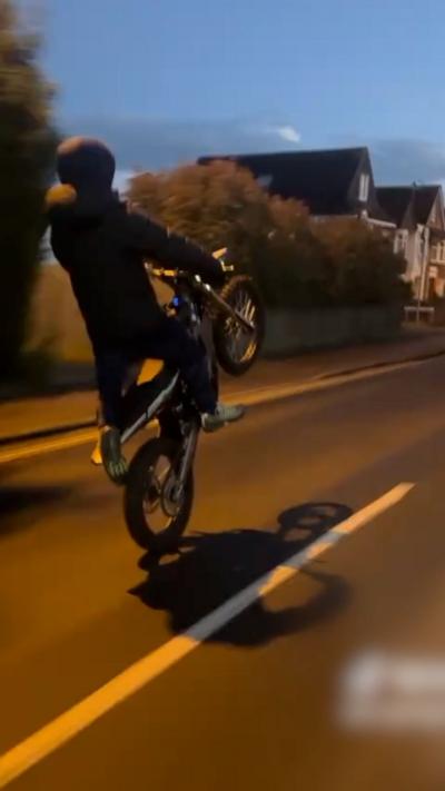 Night-time shot of an anonymous electric bike rider doing a wheelie on a road 