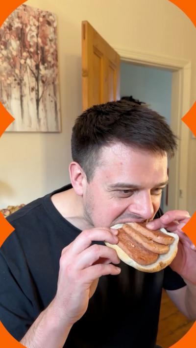 A man with short brown hair bites into a slice of white bread holding fried slices of spam.