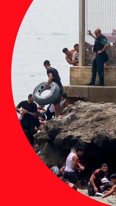 Migrants crossing rocky shoreline into Ceuta as Spanish officers watch