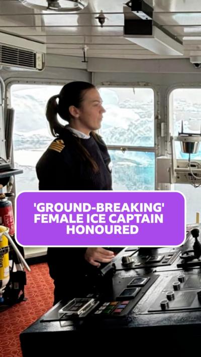 A woman in captain's uniform steering a ship. 
