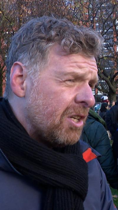 Man wearing black scarf and navy blue jacket. He has a beard and is facing side-on.