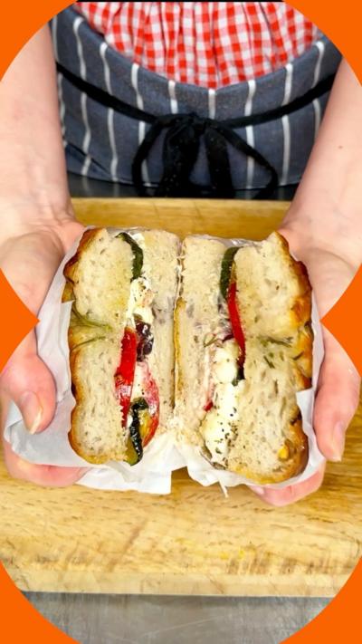 Focaccia sandwich filled with cheese and roasted vegetables, held in a pair of hands 