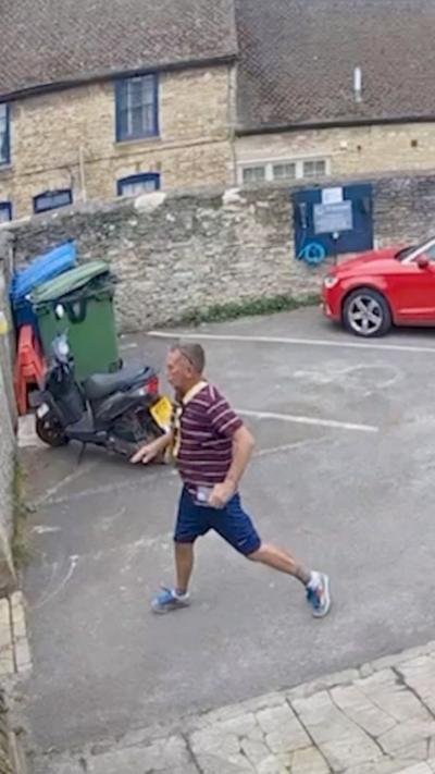 Man wearing a striped top and shorts stumbles across a car park. 