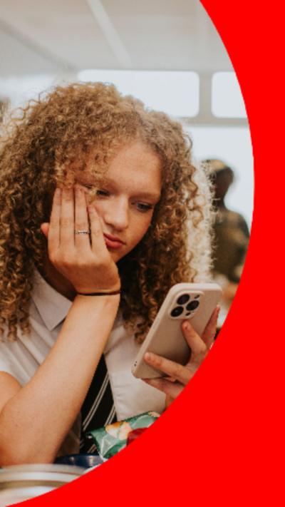 A schoolgirl rests her chin on her hand as she looks at the screen of her phone