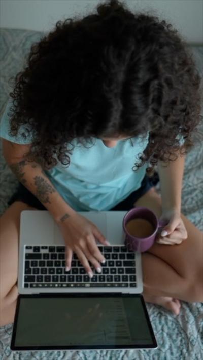 A woman with long curly hair sits with a laptop on her knee