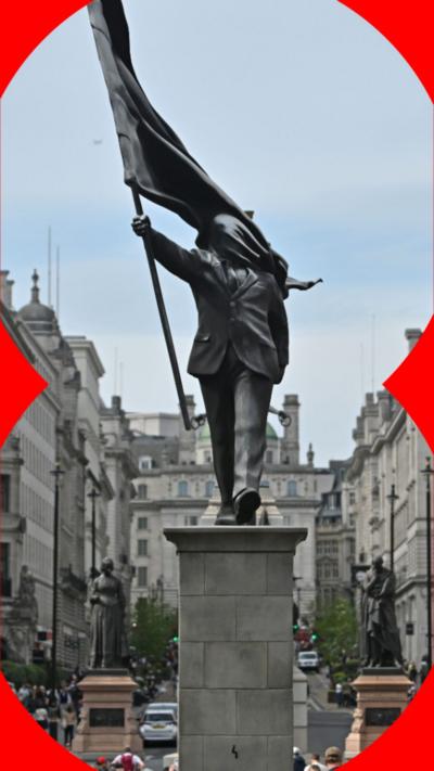 The Banksy statue is of a man holding up a flag with his right arm and the flag drapes over his face.