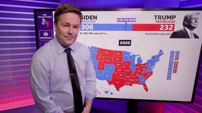 Christian Fraser standing and to his right, a touchscreen with a US map showing possible election results