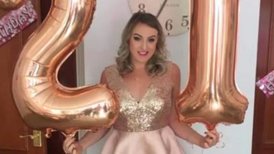 Bethan James with large birthday balloons in shape of numbers one and two wearing sequinned party dress