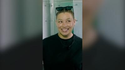 A woman smailes. She is wearing a black t shirt and has sunglasses on her head