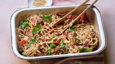 A rectangular baking tray with chilli beef noodles in and a pair of chopsticks sitting on the top