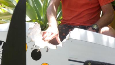 A shark teeth-sized bite in a wind surfboard next to a man with an orange shirt