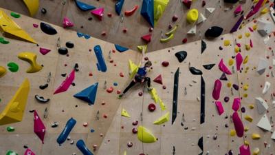 A climber, Connie Bridgens, is seen on a large indoor climbing wall with multicoloured grips