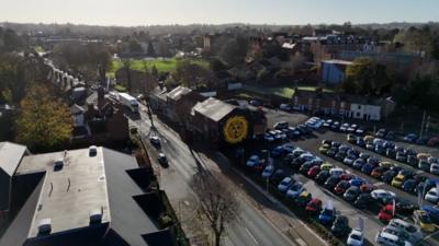 A drone image overlooking a building and car park. On a building is a yellow badge mural