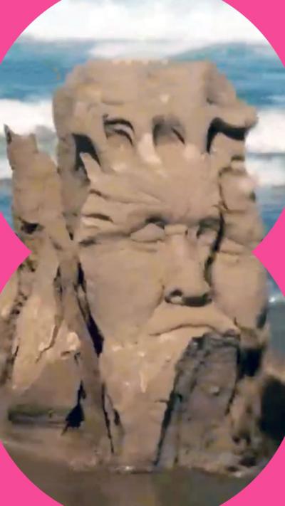 A detailed sandcastle sculpture showing a man's face. It is just on the verge of collapsing into the sea.