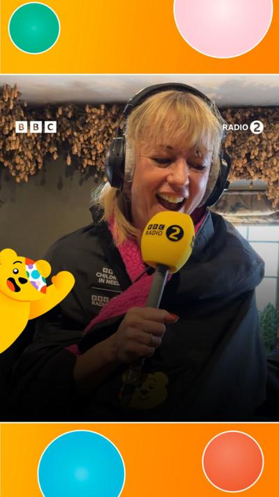 Sara Cox wears headphones and holds a Radio 2 microphone
