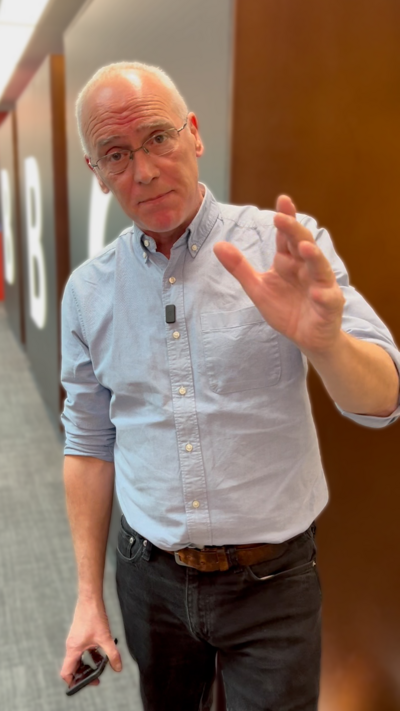 Man in blue shirt gestures towards camera.